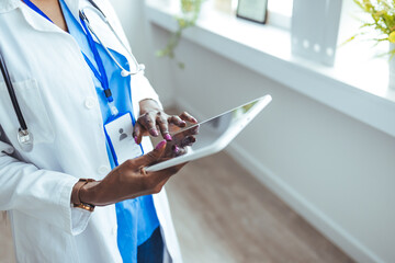 Female Doctor Wearing Scrubs In Hospital Corridor Using Digital Tablet. Doctor with stethoscope in...