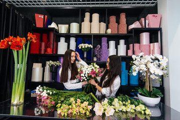 Two young women take orders and make up a beautiful festive bouquet in a cozy flower shop. Floristry and making bouquets in a flower shop. Small business.