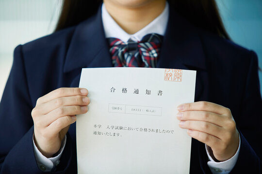 合格通知書を持ち微笑む女子学生