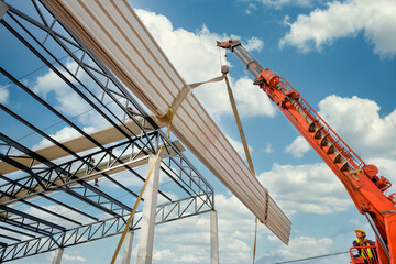 Construction workers are driving cranes to use cranes to lift large roof panels to install roofs on...