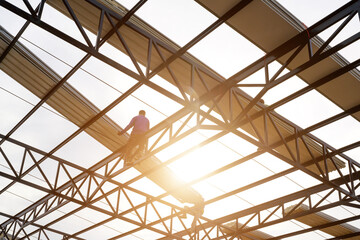 Fototapeta premium Two construction workers installing a new roof wear safety vests and safety harnesses to work on the steel roof structure.