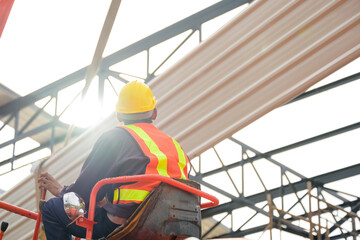 Construction workers are driving cranes to use cranes to lift large roof panels to install roofs on steel roof structures at the construction site.