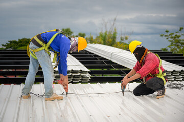 Two construction workers installing a new roof wear safety vests and safety harnesses to work on the steel roof structure. - obrazy, fototapety, plakaty