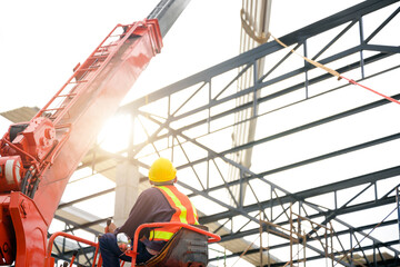 Construction workers are driving cranes to use cranes to lift large roof panels to install roofs on steel roof structures at the construction site.