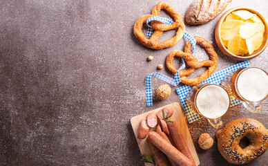Oktoberfest festival decoration symbols made from Pretzel loaf, beer, sausage, potato chips and Bavarian white and blue fabric on dark stone background.