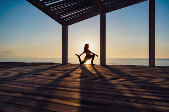 Tranquil woman doing yoga in Warrior pose during sunrise