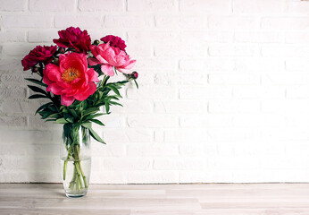 Purple peony flowers bouquet on white brick wall with copy space.