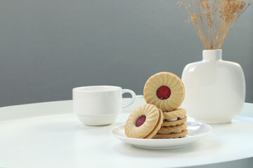homemade round cream berry cookies sandwich are on the white ceramic dish on white steel table with cup of coffee tea and white vase in the morning with background of grey cement wall background