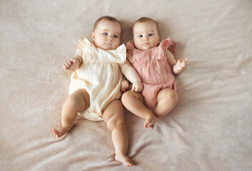 Top view of two cute baby twin girls lying together on comfortable and soft bed - obrazy, fototapety, plakaty