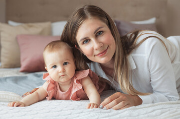 Close-up portrait of beautiful young mother with cute little baby girl lying together on soft bed at home
