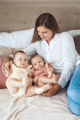 Portrait of young happy mother take care after two little twin daughters, lying together on a soft bed at home