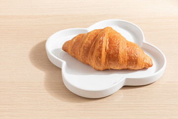 Croissant on a white plate. Isolated on wood background. Bakery menu. Breakfast. Cozy living. Food. Homemade bakery. 