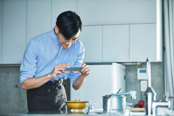 キッチンに立ちスマートフォンで料理の写真を撮る男性