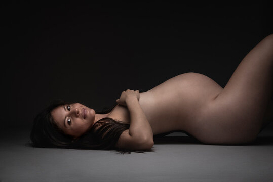 Nude pregnant woman lying down on the floor