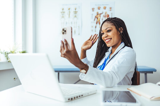 Head shot portrait woman doctor talking online with patient, making video call, looking at camera, young female wearing white uniform with stethoscope speaking, consulting and therapy concept