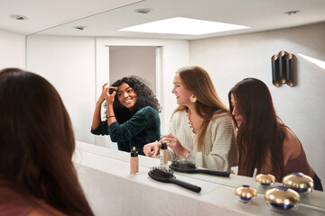 Cheerful diverse women applying makeup against mirror