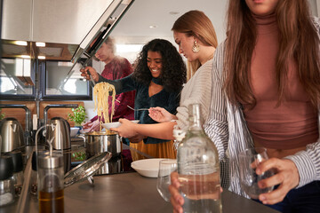 Diverse women putting spaghetti on plate in self service eatery