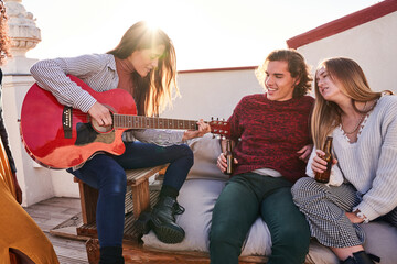 Cheerful diverse friends gathering on terrace and playing guitar