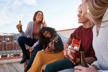 Joyful diverse friends playing guitar and ukulele on rooftop
