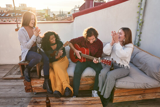 Joyful diverse friends playing guitar and ukulele on rooftop - Powered by Adobe