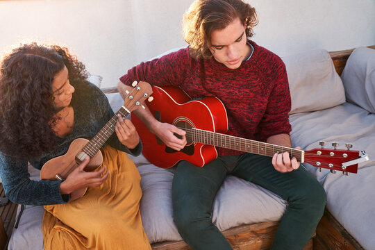 Laughing diverse friends playing guitar and ukulele on terrace - Powered by Adobe