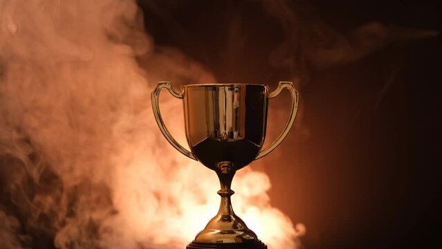 The golden trophy on a black background smokes around a fierce and fiery concept of competition or victory.