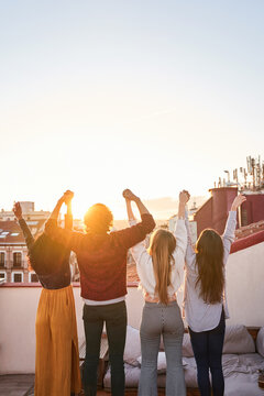 Group of unrecognizable friends celebrating and observing cityscape on terrace