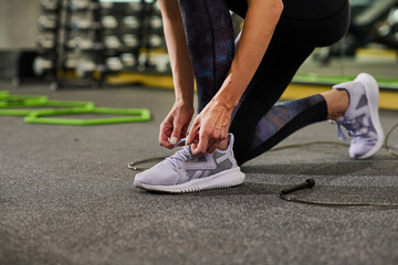 Close-up of young woman tying shoelace on her sport shoes in gym - Powered by Adobe