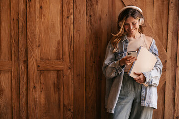 Happy young caucasian woman holding mobile phone in hand and enjoying music track. Blonde wears denim clothes spring. Concept of use