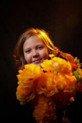 Naklejka premium Happy young small girl with bouquet yellow flowers in dark studio with flash light. Model posing on black background