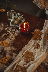 Still life in dark colors with a burning candle on the table with gingerbread cookies and...