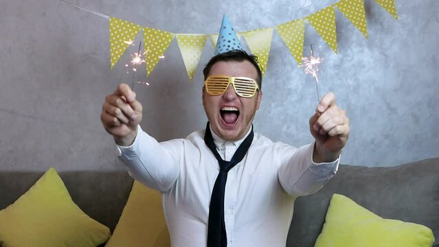 Loud smiling man happy birthday. A very happy young man celebrates his birthday, a man with begal lights in his hands, holiday garlands. An elegant man in a white shirt celebrates the holiday.
