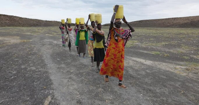 Climate change,drought,water crisis.Close-up front view.African woman walking home after collecting water in plastic containers from a volcanic spring, Turkana region, Kenya