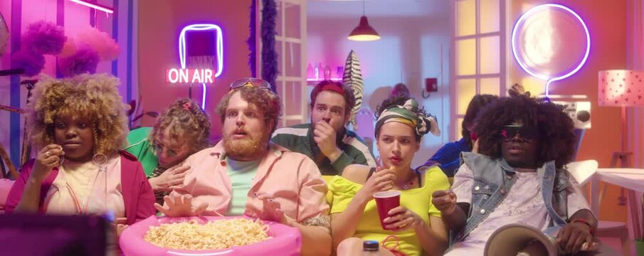 Group of diverse college friends in trendy y2k outfits watching horror movie and getting scared in party room with colorful neon light