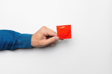 A man's hand holds a red condom in a package on a white background. High definition product....