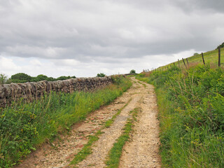 Fototapeta na wymiar Narrow dirt lane running alongside a dry stone wall surrounded hillside meadows in calderdale west yorkshire near hebden bridge