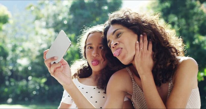 Mom and kid taking selfie with comic, funny and tongue out meme emoji face on phone for social media in summer garden together. Happy, smile and comedy mother in picture with crazy young girl at park