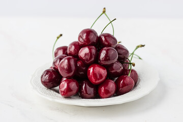 A mound of cherries on a white plate. Appetizing berries on a white background. Vitamins and a healthy lifestyle