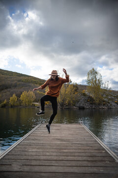Carefree woman jumping above pier near pond