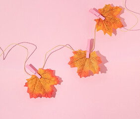 Autumn creative layout made with leaves on the rope with pink clothes hanging clips on pastel pink...