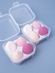Group of pink makeup soft sponges on blue background. Makeup puff in plastic case. Vertical