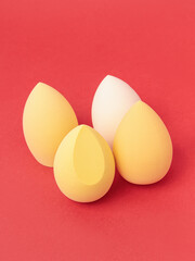 Group of yellow makeup soft sponges on red background. Makeup puff