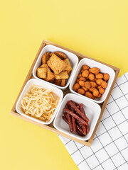 Four ceramic plates and a wooden tray on yellow background. Compartmental dish. Beer snacks. Top view