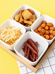 Four ceramic plates and a wooden tray on yellow background. Compartmental dish. Beer snacks closeup