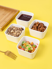 Four ceramic plates and a wooden tray on yellow background. Compartmental dish. Snacks for breakfast