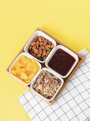 Four ceramic plates and a wooden tray on yellow background. Compartmental dish. Snacks for breakfast. Top view