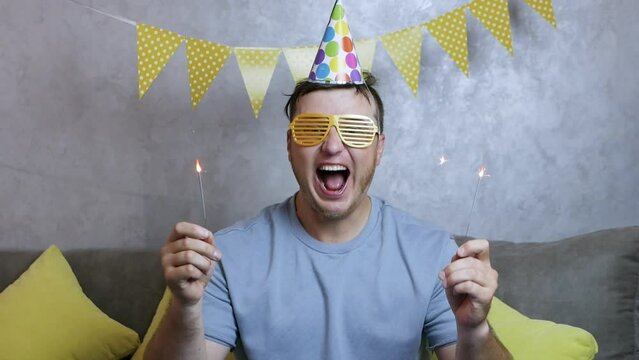 Smiling man celebrates his birthday. A very happy young man celebrates his birthday, a man with begal lights in his hands, holiday garlands