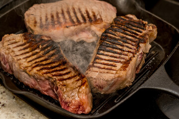 Grilling new york beef strip sirloin steaks on cast iron grill pan skillet on a electric ceramic stove counter top at home
