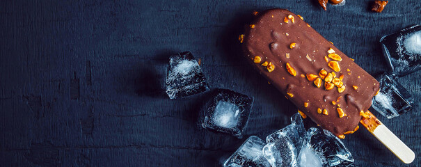 A delicious chocolate ice cream bar with almonds and ice cubes is placed on a black background.Top view