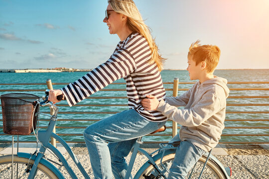 Happy family, Carefree mother and son with bike riding on beach having fun, on the seaside promenade on a summer day, enjoying vacation. Togetherness Friendly concept - Powered by Adobe